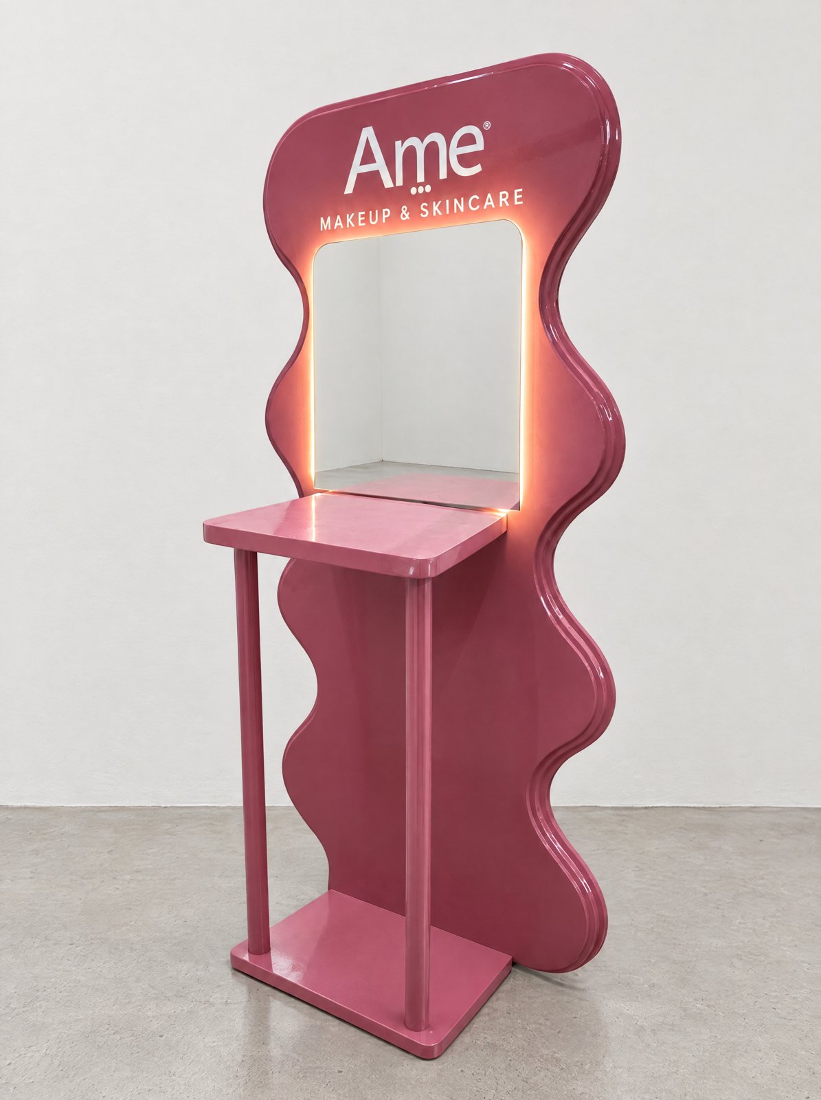 Estación de maquillaje de Ame: panel rosado de silueta ondulada con espejo iluminado y repisa