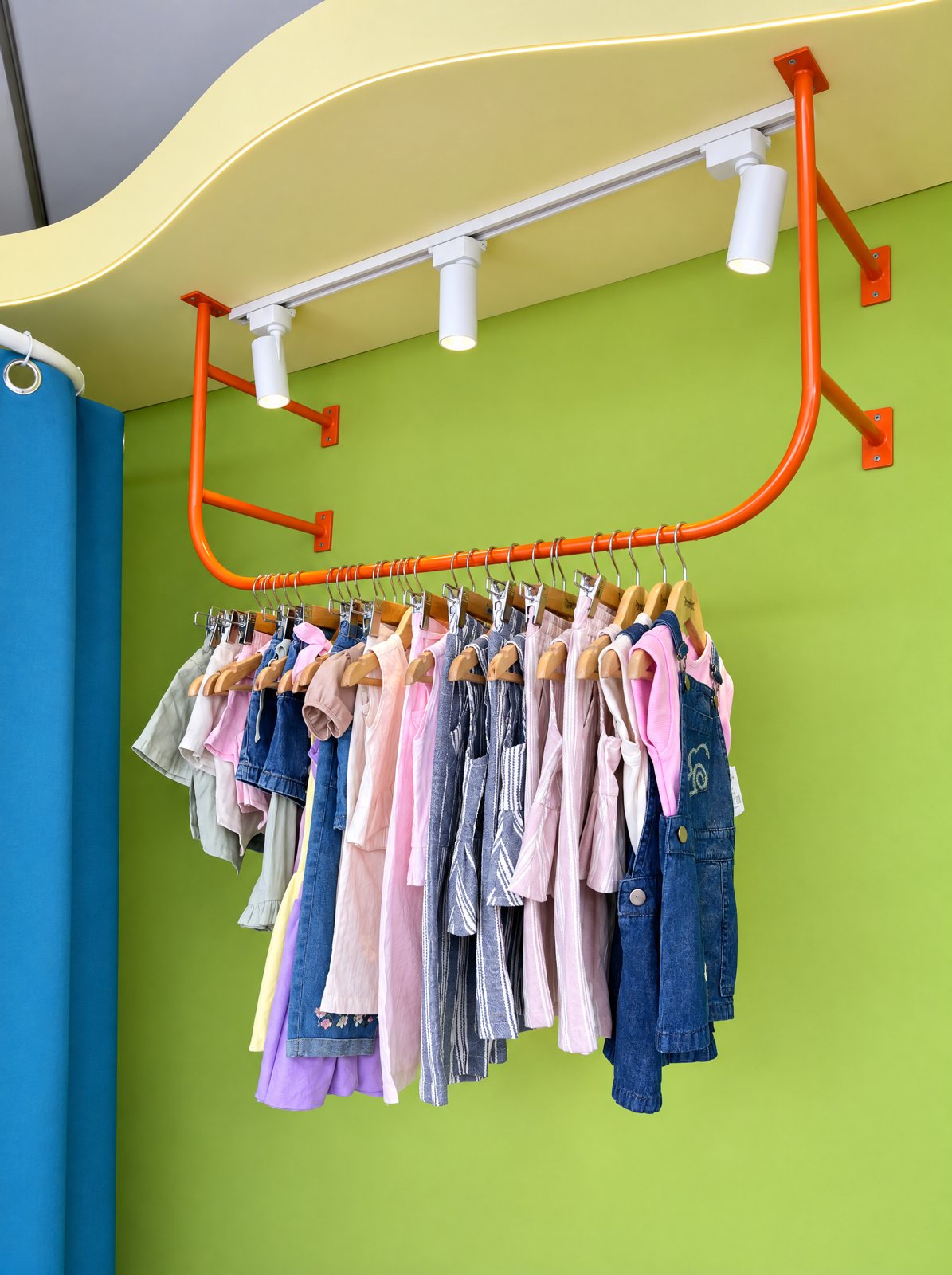Perchero naranja con ropa de niña sobre la pared verde