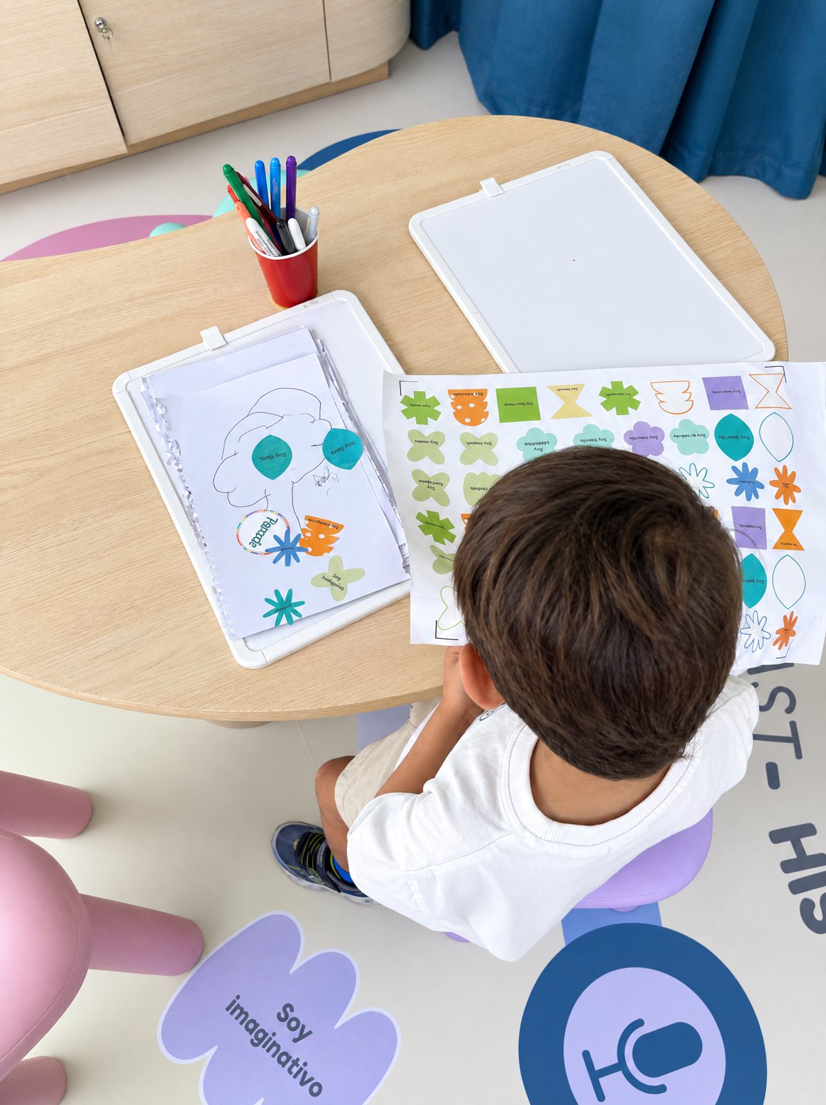 Niño armando su autorretrato con stickers en la mesa creativa